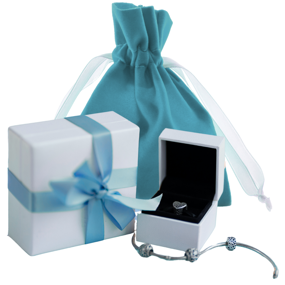 Silver bracelet and ring in an open jewelry box with a white gift box featuring a blue ribbon and a blue fabric gift bag. 