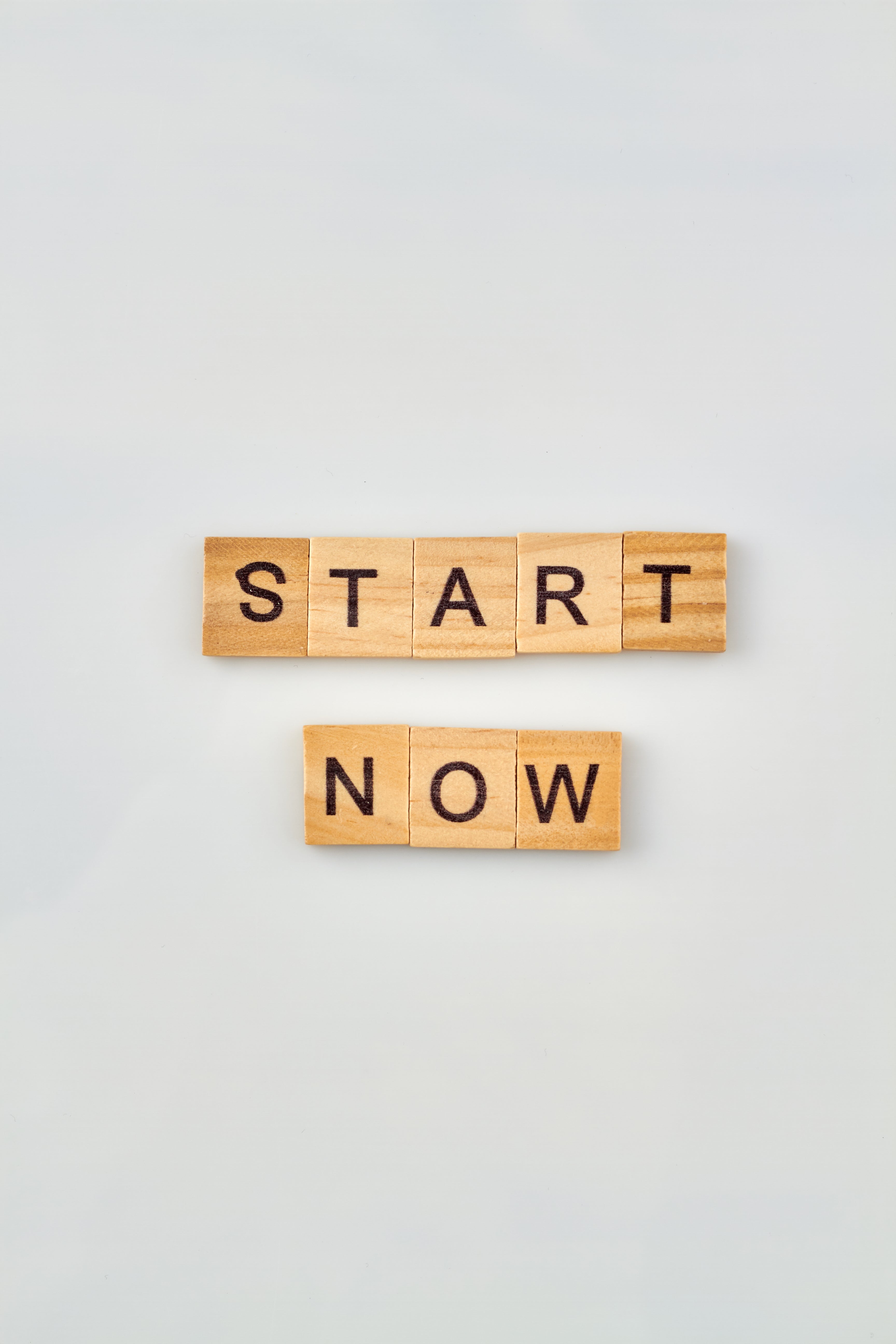 Wooden blocks with letters spelling START NOW on a light gray background